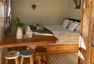 Gezellige glampingaccommodatie bij Lima Escape Boomlodges met bed, houten tafel en zonlicht binnen.