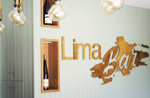 Interior of Lima Escape Bar in Portugal featuring wine bottles and a stylish Lima Bar sign on a pale wall.