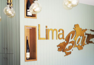 Interior of Lima Escape Bar in Portugal featuring wine bottles and a stylish Lima Bar sign on a pale wall.