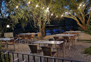 Charming Lima Escape glamping terrace with tables, chairs, and string lights under trees in the evening.