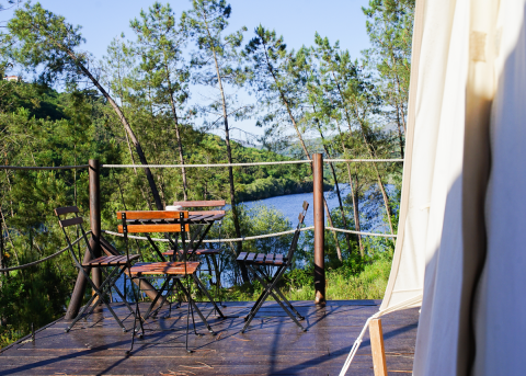 Terrasse med bord og stole ved Lima Escape Boomlodges Glamping, udsigt over flod og skov i Portugal.