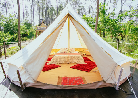 Alojamiento glamping en tienda con cómoda cama y alfombras rojas en un bosque verde de Portugal.