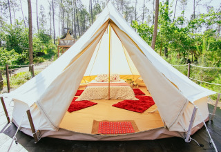 Comfortabele glamping tent met tweepersoonsbed en rode tapijten omgeven door bossen in Portugal.