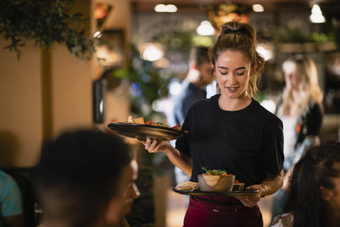 Una cameriera serve cibo agli ospiti in un ristorante accogliente di un villaggio vacanze con glamping.