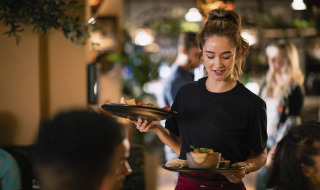 Una camarera sirve comida a los comensales en un restaurante acogedor de un parque de vacaciones con glamping.