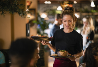 A waitress serves food to guests at a cozy restaurant in a holiday park offering glamping accommodations.