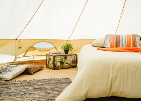 Interno di tenda glamping in Portogallo con letto comodo, cuscini colorati e tappeto intrecciato.