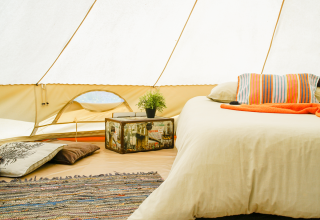 Interior de tienda glamping en Portugal con cama cómoda, alfombra, baúl vintage y cojines.