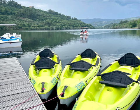 Four yellow kayaks tied to a dock on a serene river with green hills, at Lima Escape Glamping in Portugal.