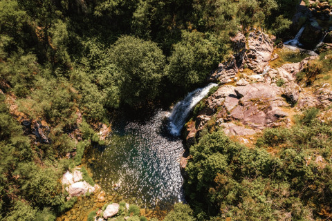 Aerial view of Lima Escape Boomlodges and glamping tents in Portugal, nestled by lush forest and a waterfall.