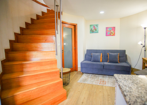 Gemütlicher Innenraum mit Holztreppe, grauem Sofa, bunten Kissen und Dekor im Lima Escape Glamping.