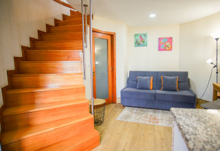 Gemütlicher Innenraum mit Holztreppe, grauem Sofa, bunten Kissen und Dekor im Lima Escape Glamping.