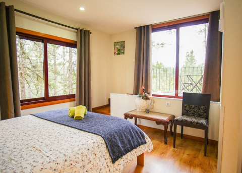 Cozy bedroom at Lima Escape glamping in Portugal, featuring large windows with a tranquil forest view.