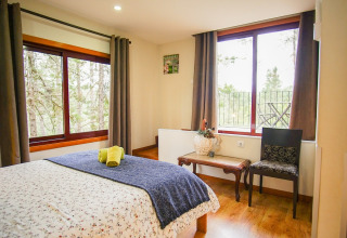 Chambre douillette au glamping Lima Escape au Portugal, avec grandes fenêtres et vue sur la forêt paisible.