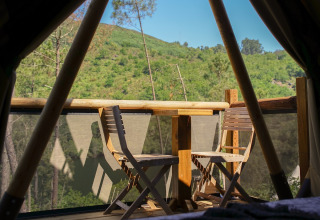 Vista desde una tienda glamping con muebles de madera y colinas verdes en Lima Escape Boomlodges, Portugal.