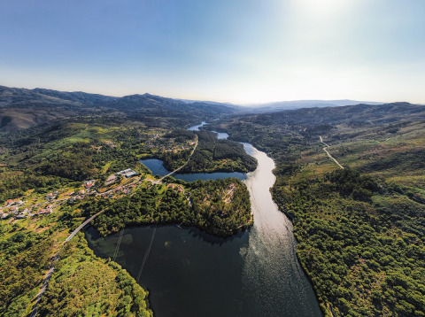 Luftfoto af Lima Escape Boomlodges og glamping telte i Portugal med flod og grønne bakker i landskabet.