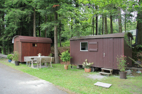 Dos pequeñas cabañas de madera y un banco en Camping Isny, alojamiento glamping de lujo en Baden-Württemberg.