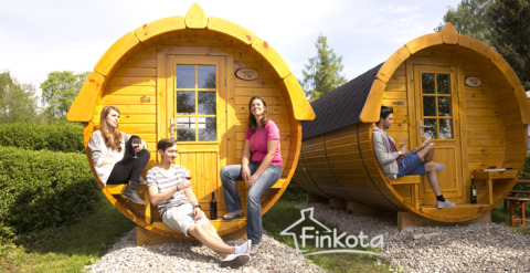 Vier jongeren genieten voor tonvormige glampingaccommodaties op Camping Isny, Baden-Württemberg, Duitsland.