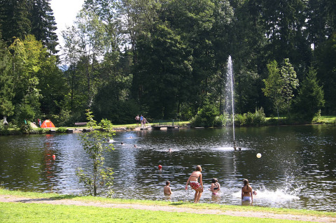 Camping Isny - Luxe glamping Baden-Württemberg con bambini che nuotano nel lago e tenda tra gli alberi.