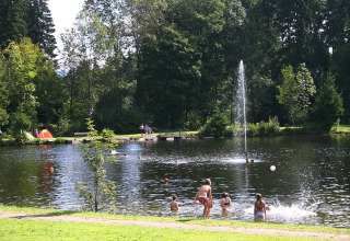 Camping Isny - Luxe glamping Baden-Württemberg mit Kindern, die im Badesee schwimmen und Zelt am Ufer.