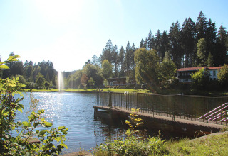 Idyllischer See mit Steg und Unterkünften im Hintergrund bei Camping Isny - Luxe glamping Baden-Württemberg.