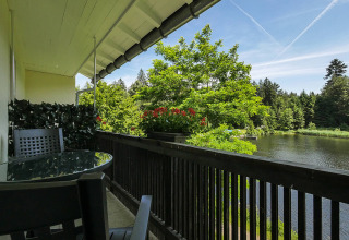 Udsigt fra altan med bord, stole og blomsterkasse over mod sø og grøn skov ved Camping Isny - Luxe glamping Baden-Württemberg.