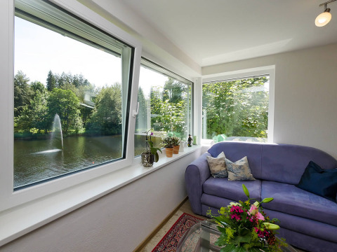 Indvendig udsigt fra luksus glamping ved Camping Isny, med sofa, blomster og udsigt til sø og springvand.