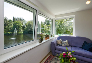 Innenraum von Luxe Glamping bei Camping Isny mit Sofa, Blumen und Ausblick auf See mit Springbrunnen.