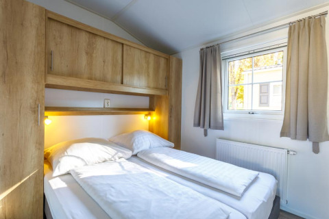 Schlafzimmer mit Doppelbett, Holzschränken und Fenster in einer Glamping-Unterkunft bei Camping Pilsensee.