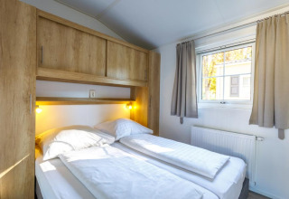 Soveværelse med dobbeltseng, store træskabe og vindue i et glamping-ophold på Camping Pilsensee.