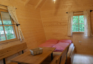 Intérieur d’une cabane en bois à Boomhutpark Voglsam avec lit, table, banc et vue sur la nature.