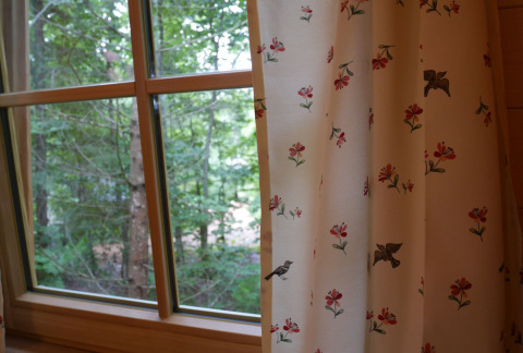 View from a treehouse window with floral curtains at Boomhutpark Voglsam - Boomhutten Beieren glamping site.