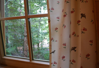 Vista desde una ventana de casa árbol con cortinas florales en Boomhutpark Voglsam - Boomhutten Beieren.