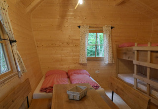 Interno accogliente di una casetta in legno al Boomhutpark Voglsam, Baviera, con letto doppio e a castello.