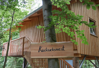 Wooden treehouse with 'Kuckucksnest' sign in the forest at Boomhutpark Voglsam, Bavaria, glamping site.