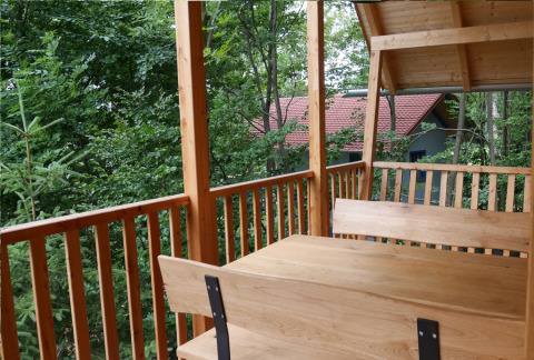 Vue du balcon d’une cabane sur pilotis à Boomhutpark Voglsam, avec table et bancs en bois, forêt autour.