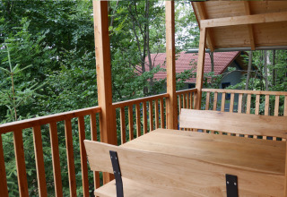 Zicht vanaf het balkon van een boomhut in Boomhutpark Voglsam, met houten tafel, banken en bosgebied.