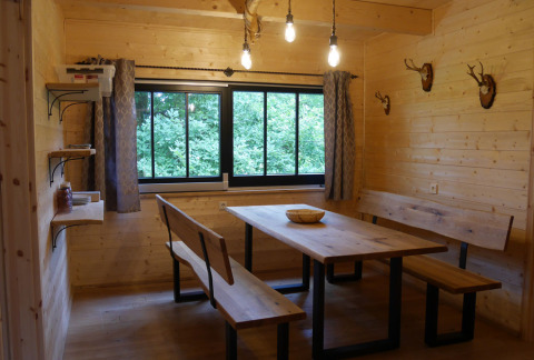 Eethoek in houten glamping hut met banken, tafel, uitzicht op het bos en geweien aan de wand gemonteerd.