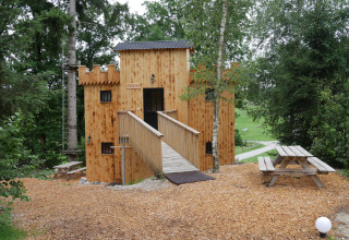 Træhytte glamping indkvartering formet som et slot i Boomhutpark Voglsam, omgivet af skov og picnicborde.