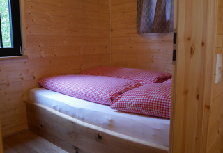 Slaapruimte in een boomhut van Boomhutpark Voglsam met geruit beddengoed en houten wandpanelen.