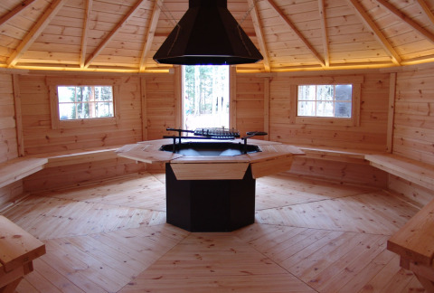 Binnenkant van een houten boomhut in Boomhutpark Voglsam met zitbanken en een centrale haard.