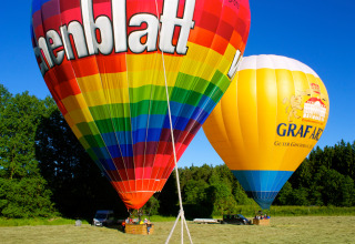 Zwei bunte Heißluftballons bereit zum Start auf einer Wiese bei Boomhutpark Voglsam in Bayern.