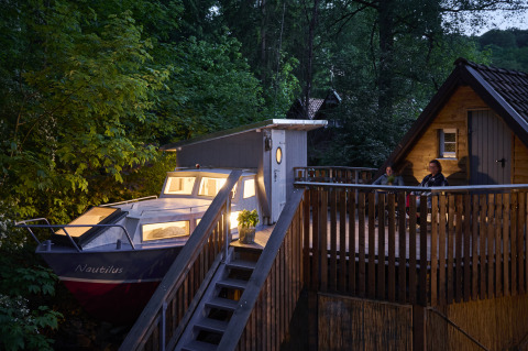 Glamping-Unterkunft im Baumschiffhotel Boomschepen Beieren mit Boot und Terrasse am Waldrand.