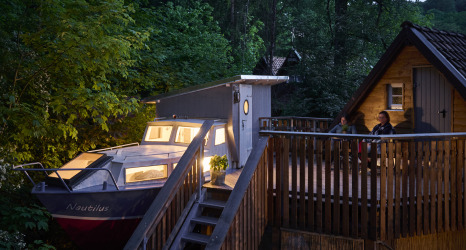 Glamping-Unterkunft im Baumschiffhotel Boomschepen Beieren mit Boot und Terrasse am Waldrand.