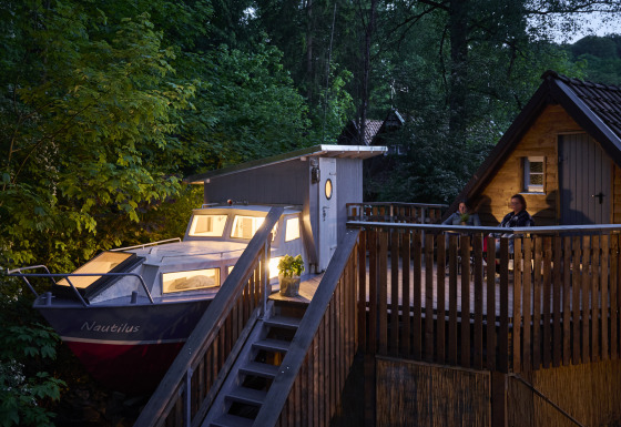 Hébergement glamping au Baumschiffhotel Boomschepen Beieren avec bateau, terrasse et cabane en forêt.