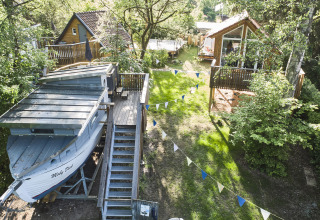 Alojamiento glamping original con barco Baumschiffhotel, cabañas de madera y banderines en plena naturaleza.