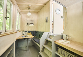 Knusse binnenkant van Baumschiffhotel glamping in Beieren met tafel, bank en trapje zichtbaar.