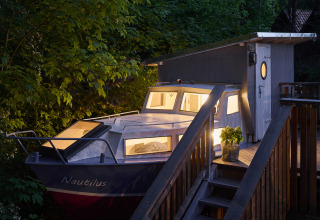 Avondbeeld van Baumschiffhotel - Boomschepen Beieren glamping, bootvormige hut tussen groene bomen.