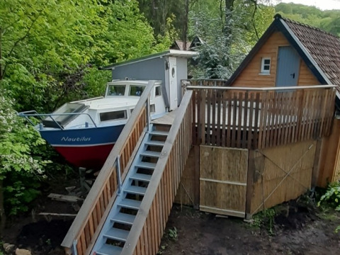 Alojamiento glamping único en Baumschiffhotel con barco y cabaña sobre plataforma de madera en el bosque.