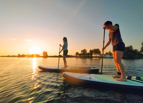Dos personas practicando paddle surf al atardecer en un lago en Camping Natuurlijk de Veenhoop en Frisia.